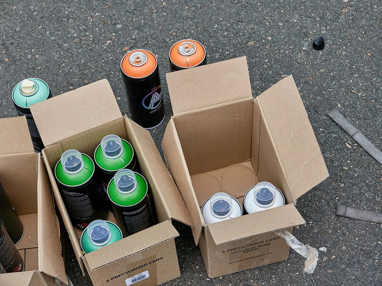 Bombes de peinture vertes, blanches et orange dans des cartons ouverts posés sur l’asphalte