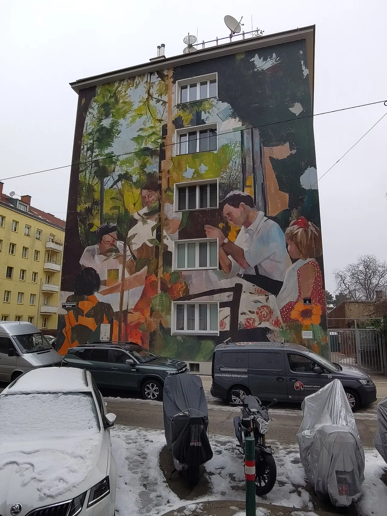 Façade d’immeuble couverte d’une fresque réaliste montrant une famille attablée dans un jardin