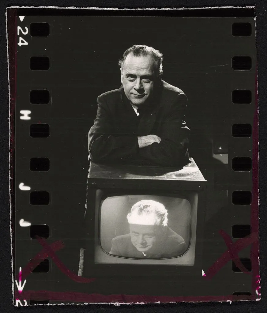 Marshall McLuhan appuyé sur un téléviseur qui diffuse sa propre image, photo noir et blanc
