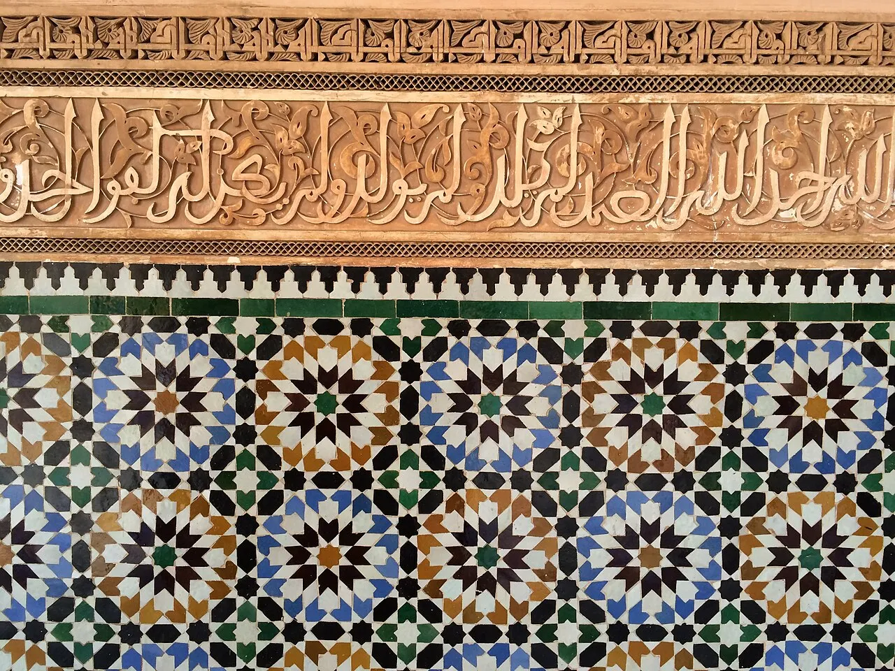 Mosaïque de zellige à étoiles géométriques bleues, vertes et brunes sous une frise calligraphiée en stuc