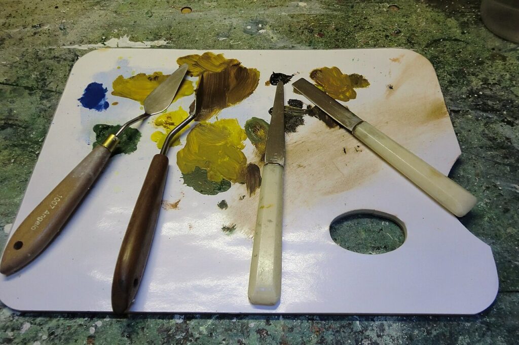 Quatre couteaux à peindre et à palette posés sur une palette couverte de peinture à l'huile